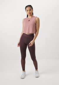 Lyserød crop top med sort logo, parret med mørkebourgogne høj talje leggings med sideindsatser og en glat tekstur.