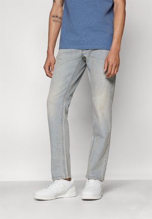 Lysblå denimjeans med lige ben, недbrudt struktur og fem-lomme design. Båret med en blå t-shirt og hvide sneakers.