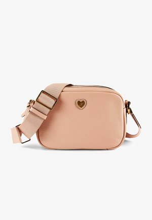 Petit sac bandoulière rectangulaire beige avec une large sangle réglable et un petit emblème doré en forme de cœur à l'avant.