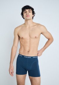 Navy blue boxer briefs with a flexible waistband featuring "BJÖRN BORG" branding. Smooth fabric, form-fitting design, and mid-thigh length.