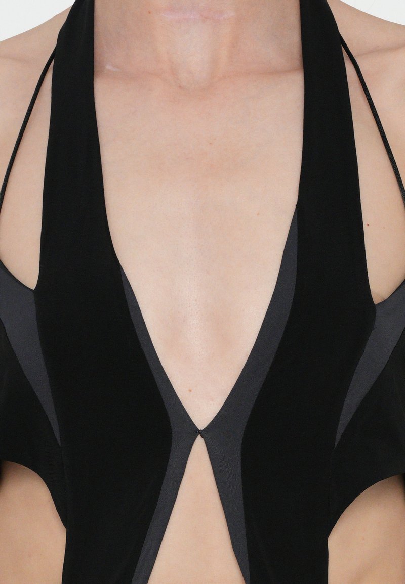 Black halter-neck garment with a deep V-neckline, featuring smooth texture and contrasting black side panels, showing skin through cutouts.