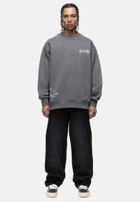 Grijze sweatshirt met een oversized pasvorm, ronde hals en een grafische print aan de voorkant. Gecombineerd met losse zwarte denim broek en zwart-witte sneakers.