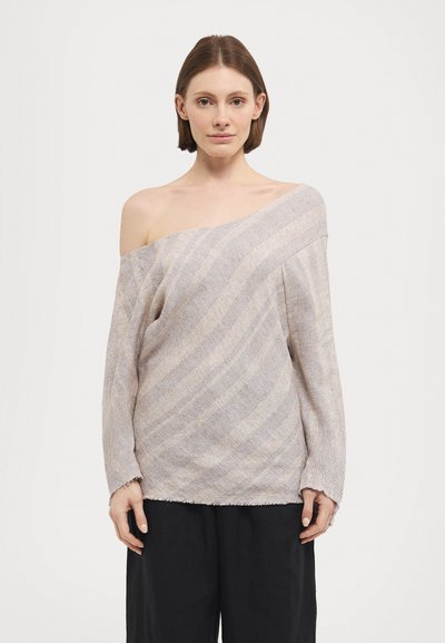 Šviesiai bežinė off-shoulder megztinis su įstrižais raštais, laisvas kirpimas, ilgomis rankovėmis ir suplyšusiomis apdailos detalėmis. Sujungtas su laisvais juodais kelnių.