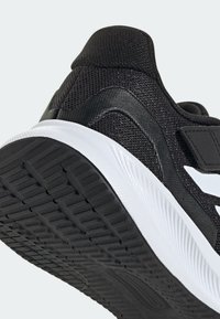 Scarpa sportiva nera con tomaia in mesh testurizzato, intersuola bianca e suola in gomma con motivo, dotata di un collare imbottito robusto e branding minimale.