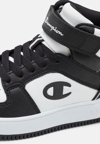 Czarno-białe sneakersy wysokie, wykonane z materiałów skórzanych i syntetycznych. Posiadają wyściełany kostkę, teksturowane logo oraz kontrastujące sznurówki. Płaska podeszwa.