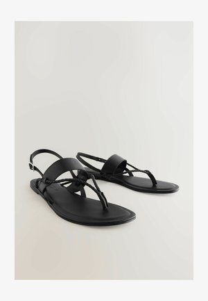 Fekete szandálok lapos talppal, fonott lábujjpántokkal és széles bokapántokkal. Simább anyagból készült, állítható csat részlettel.