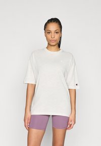 Ανοιχτό γκρι υπερμεγέθη μπλουζάκι με κοντά μανίκια και μικρό λογότυπο στο στήθος. Συνδυασμένο με βερμούδες ποδηλασίας σε λιλά απόχρωση. Ομαλή υφή υφάσματος.