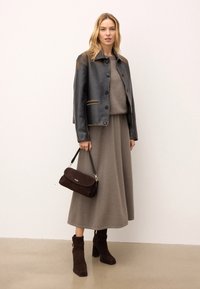 Czarna skórzana kurtka z jasnym przeszyciem, szary sweter dzianinowy, szara spódnica maxi, ciemnobrązowa zamszowa torebka, oraz brązowe botki na stabilnym obcasie.