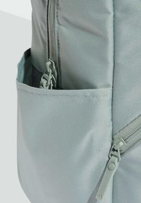 Light grey backpack with a textured finish, featuring a side pocket and a zip closure with matching hardware.