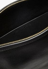 Gros plan de l'intérieur d'un sac en cuir noir avec des dents de fermeture éclair dorées visibles et le nom de la marque embossé sur la doublure.