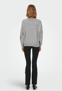 Grauer gestrickter Pullover mit lockerer Passform, runder Halslinie und langen Ärmeln. Schwarze, ausgestellte Hose mit glatter Oberfläche, getragen mit Stiefeletten.