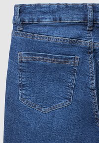 Jeans in denim blu con una tasca posteriore caratterizzata da una cucitura arancione a contrasto, dalla forma strutturata e dalla texture liscia.