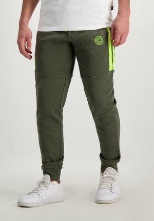 Olijfgroene joggers met gele zijstrepen, gemaakt van zacht materiaal. Heeft een ronde logo op de linker dij en cuffs aan de enkels.