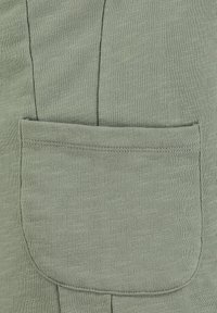 Acercamiento a un bolsillo de tela verde salvia con costuras visibles y un patrón de punto texturizado.