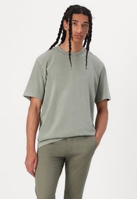 T-shirt vert olive clair à manches courtes avec une coupe décontractée, col rond et texture douce, accompagné d'un pantalon ajusté assorti.