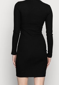 Vestido negro de manga larga con canalé, de silueta ajustada, con dobladillo a la altura de la rodilla y diseño sin costuras, que muestra una textura suave en toda su superficie.