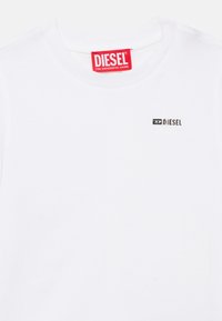 Λευκό βαμβακερό μπλουζάκι με στρογγυλή λαιμόκοψη, με κόκκινη ετικέτα στον γιακά και μικρό μαύρο λογότυπο 'DIESEL' στην μπροστινή αριστερή πλευρά.