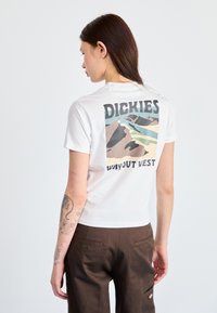Bílá bavlněná tričko s grafikou na zadní straně zobrazenou hory a textem "DICKIES WAY OUT WEST" v černých a modrých akcenty.