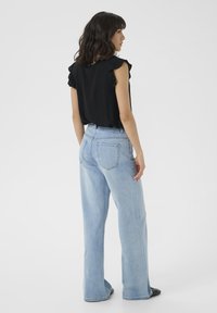 Haut noir avec des manches volantes associé à un jean bleu clair taille haute évasé ; tissu lisse, coupe décontractée et poches basiques.