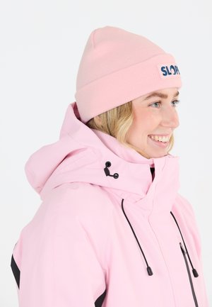 Pink vandtæt jakke med hætte, der har justerbare snore og en sort detalje. Båret med en matchende pink strikhue.
