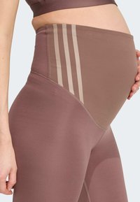 Leggings de grossesse dans un ton brun discret, avec une taille haute et des rayures beige clair sur le côté. Tissu lisse et extensible.