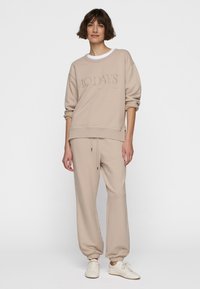 Lichtbeige sweatshirt met "10 DAYS" in bijpassende tint; gecombineerd met beige joggers met elastische boorden en een verstelbare tailleband. Witte schoenen.