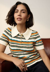 Pletené polo tričko s pruhy v oranžové, modré a hnědé barvě. Má krátké rukávy, krémový límec a zapínání na knoflíky. Vylepšená textura.