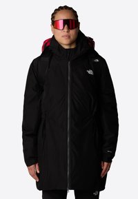 Svart vanntett parka med glidelås foran, justerbar midje og hette. Har The North Face-logoen på brystet og svart stoff med en glatt tekstur.