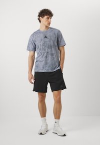 T-shirt en gris tie-dye avec un logo noir, associé à un short de sport noir avec des poches latérales et des accents noirs. Des baskets blanches complètent le look.