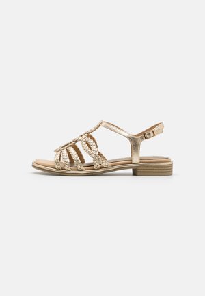 Gold leather sandals with braided upper design and open toe, featuring a low heel and adjustable ankle strap for secure fit.