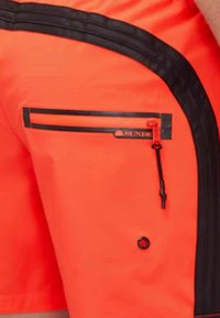 Pantaloni corti arancioni con una tasca con zip nera e dettagli neri. Presentano un design elegante, una texture liscia e un logo sulla tasca.