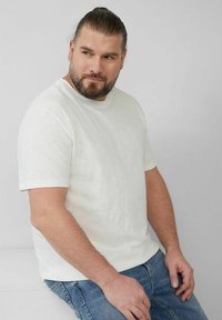 White short-sleeve t-shirt made of textured fabric, paired with blue jeans. Features a relaxed fit and round neckline.