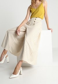 Ärmlös gul topp kombinerad med vida, randiga byxor i kräm och guld med knappar. Vita klackskor med slingback-design.