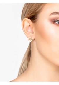 Orecchini in tono dorato con un design a trifoglio e un centro aperto, impreziositi da piccole pietre trasparenti lungo il contorno.