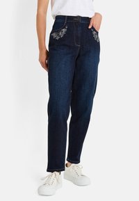Jeans de mezclilla de un azul oscuro con bordado decorativo en blanco de flores en los bolsillos, diseño de pierna recta y un clásico cierre de botón y cremallera.