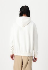 Sudadera blanca con capucha y manga larga, de tela suave; cuenta con un bolsillo canguro y un corte relajado.