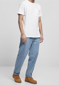 Bílý bavlněný tričko s kapsou na hrudi, spárované se světle modrými džínami a béžovými šněrovacími botami s semišovými detaily a gumovými podrážkami.