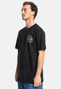 Black cotton t-shirt with short sleeves, featuring a small white graphic design on the left chest. Relaxed fit, smooth texture.