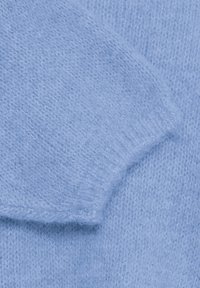 Détail de la manche d'un pull en tricot bleu clair avec une texture douce, des poignets côtelés et une finition lisse, mettant en valeur la délicatesse du tissu.
