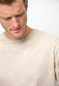 Beige t-shirt med rund hals i mjukt tyg, med ett subtilt strukturerat mönster och en slät yta. Halsringningen är av klassisk ribbad stil.