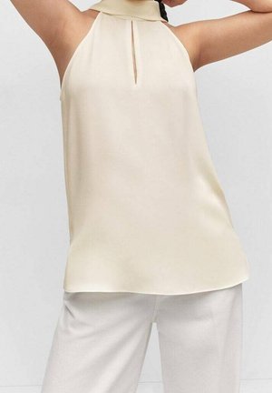 Haut sans manches en tissu beige clair avec une fente en trou de serrure au niveau du cou. Texture lisse et coupe décontractée, associé à un pantalon de couleur claire.