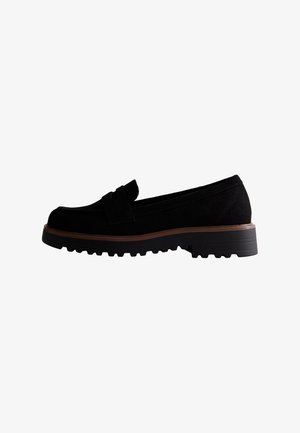 Mocassins en daim noir avec une semelle en caoutchouc plate, ornés d'un nœud décoratif et d'une bordure de semelle intermédiaire marron pour le contraste.