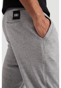 Grey sweatpants made of soft fabric, featuring an elastic waistband, side pockets, and a black logo patch on the back.