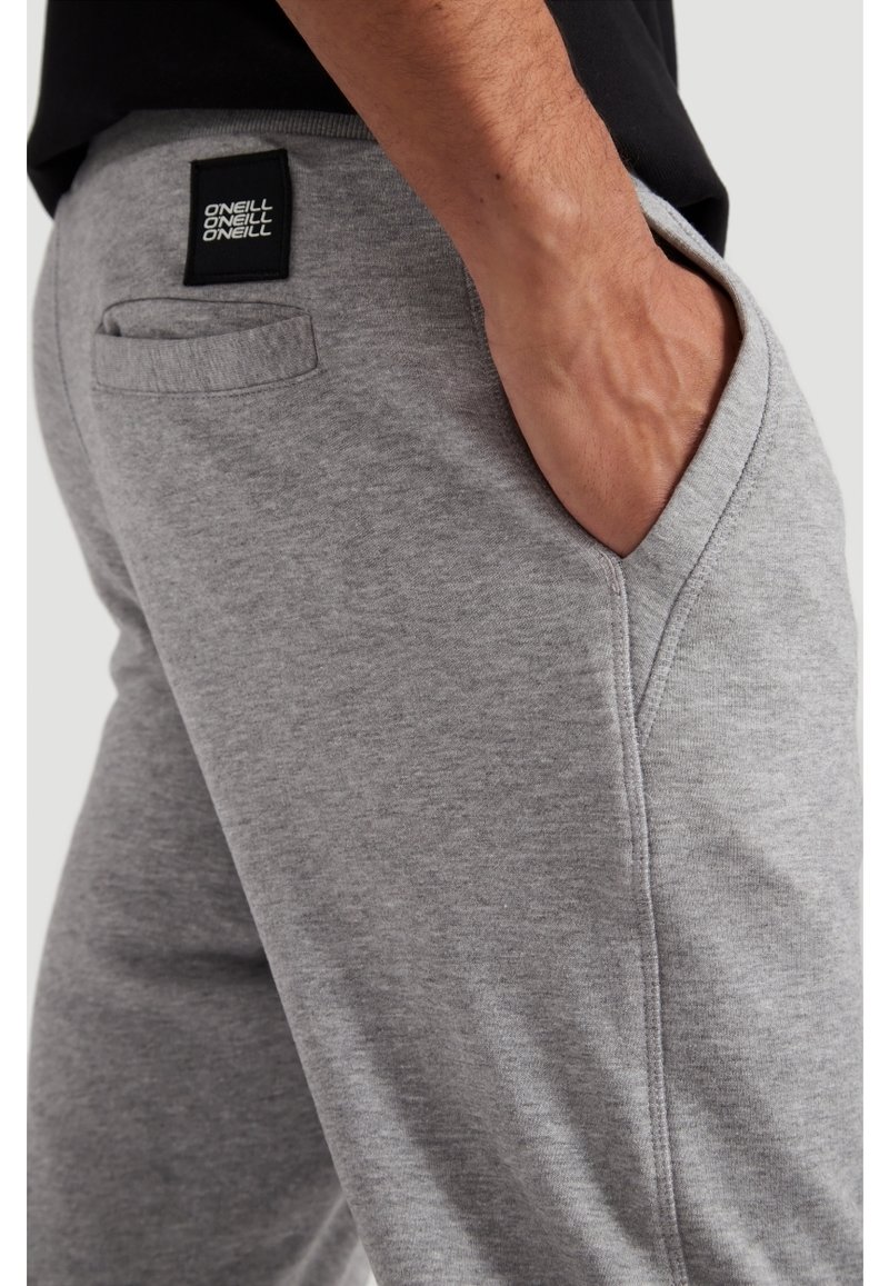 Pantaloni da tuta grigi realizzati in tessuto morbido, con vita elastica, tasche laterali e una toppa con logo nero sul retro.