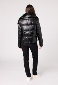 Zwarte pufferjack met opgeblazen secties, glanzende afwerking, hoge kraag en lange mouwen, gecombineerd met zwarte jeans en witte sneakers.