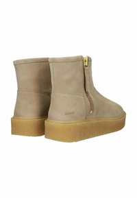 Botines de ante beige con cremallera lateral y herrajes dorados, que cuentan con una suela de plataforma texturizada. Diseño minimalista con líneas limpias.
