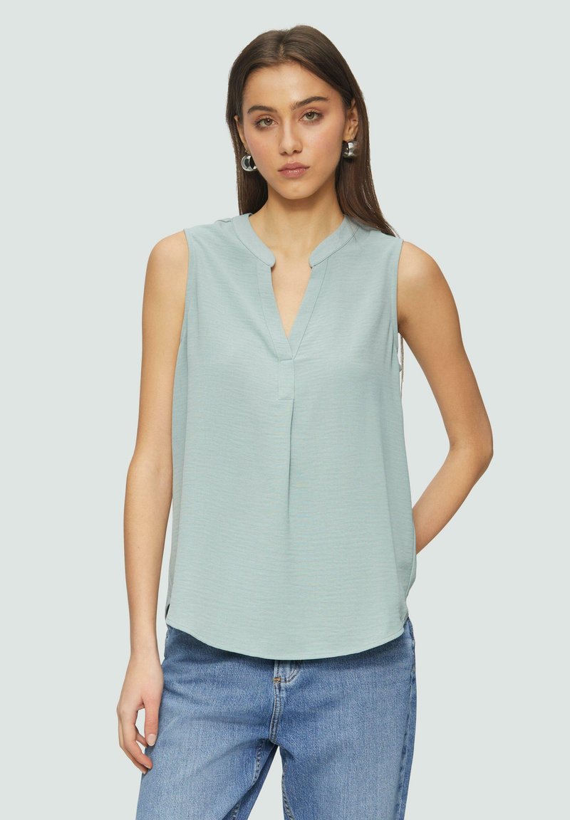 Helles blaues ärmelloses Oberteil mit V-Ausschnitt, feiner Textur und abgerundetem Saum. Kombiniert mit hochgeschnittenen Jeans für einen lässigen Look.
