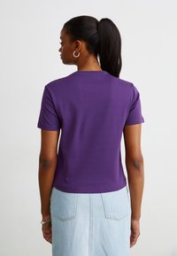 Camisa morada de manga corta con un cuello redondo acanalado, textura suave y un diseño ligeramente recortado, combinada con una falda de mezclilla azul claro.