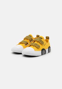 Gule lerretsk sneakers med svarte og gule stripete borrelåsremmer, hvite gummitupper og en teksturert svart og grå mønstrete såle.