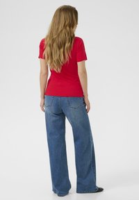 T-shirt rouge à manches courtes associé à un jean bleu ample, montrant une texture en denim classique. La tenue présente des lignes de design simples.